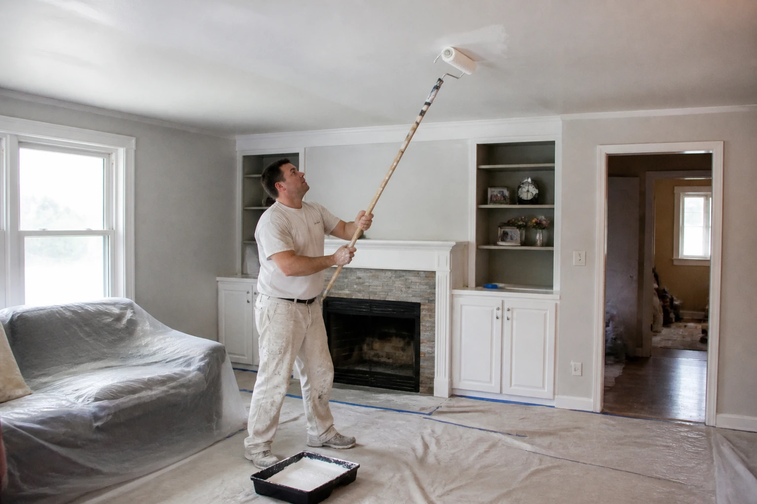 Peintre amateur appliquant de la peinture blanche au rouleau sur un plafond avec une perche télescopique