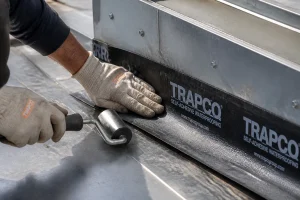 Pose d'une bande Trapco auto-adhésive sur jonction de toiture plate, gros plan sur la mise en œuvre