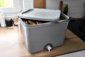 Seau bokashi hermétique avec robinet de vidange posé dans une cuisine, couvercle entrouvert