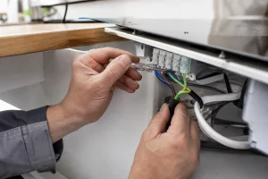 Électricien raccordant les fils d'une plaque à induction à un bornier 32A sous un plan de travail