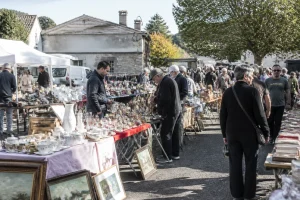 Vide-greniers avec stands d'exposants et visiteurs chinant entre les allées un matin ensoleillé