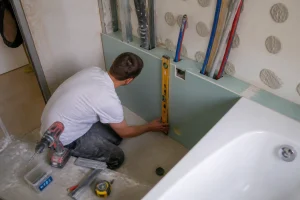 Artisan posant une plaque de placo en coffrage sans rail autour d'un tuyau de salle de bain