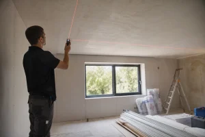 Artisan mesurant un plafond avant la pose d'une toile tendue avec un mètre laser